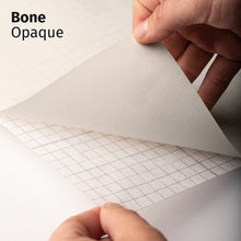 Cargar imagen en el visor de la galería, Bone Opaque adhesive textile film with grid-lined non-woven backing, shown being peeled back to demonstrate its opaque appearance and easy application.